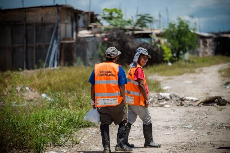 Two people in orange vests implementing disaster risk reduction measures while walking down a dirt road.