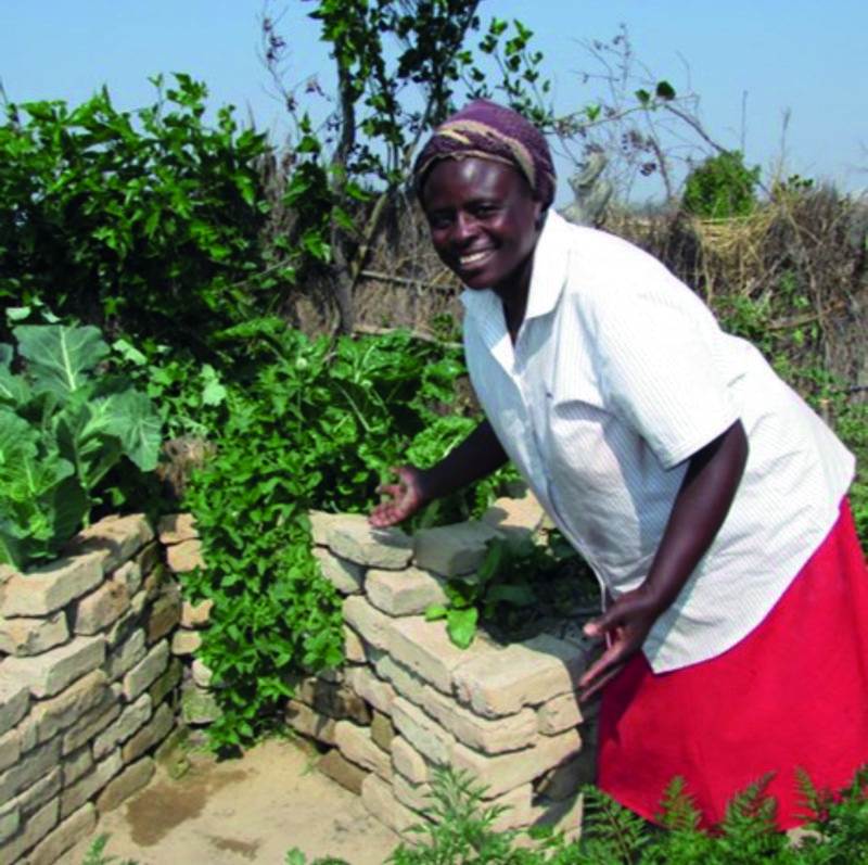 A woman creating her own keyhole garden beside a brick wall.
