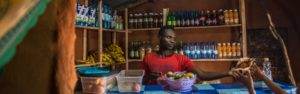 A man is standing in front of a small shop promoting Renewable Energy for Refugees (RE4R).