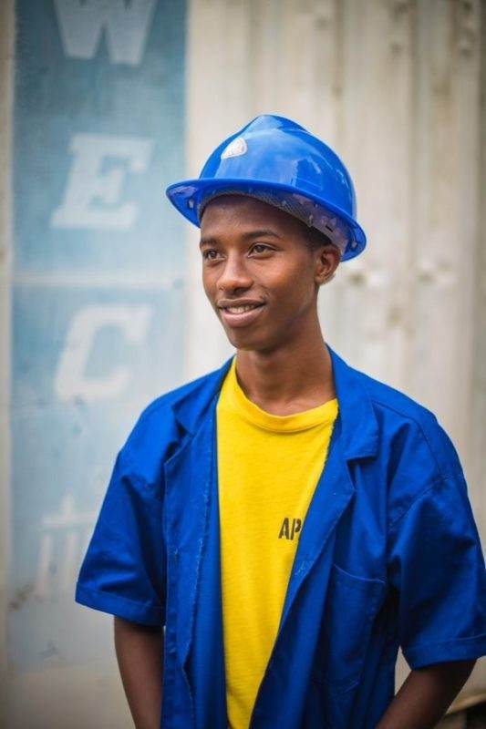 A young man wearing a blue hard hat at a Renewable Energy for Refugees (RE4R) project site.