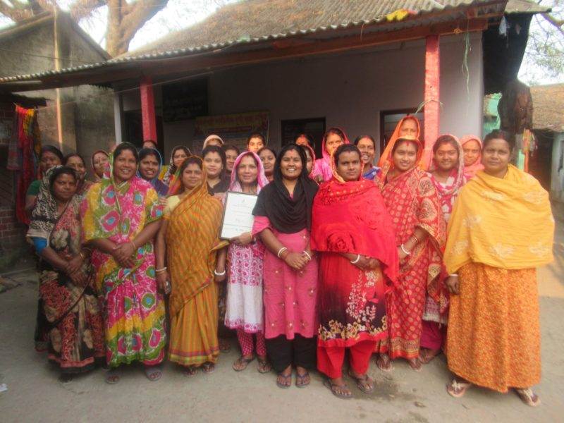 A group of women in colorful saris builds futures together by standing in front of a house.
