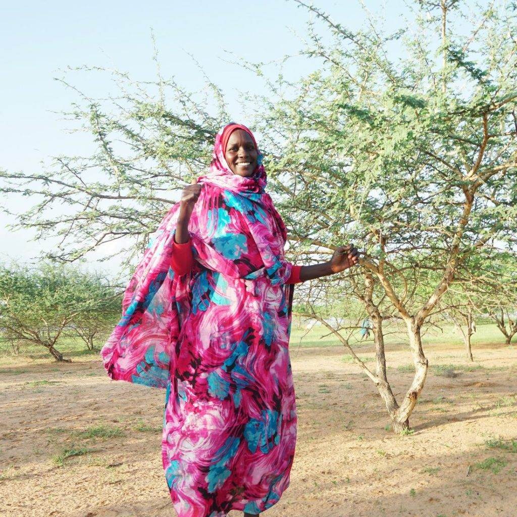 A woman in a colorful dress standing in an orchard.