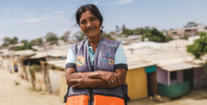 A woman in an orange vest standing in front of shacks.