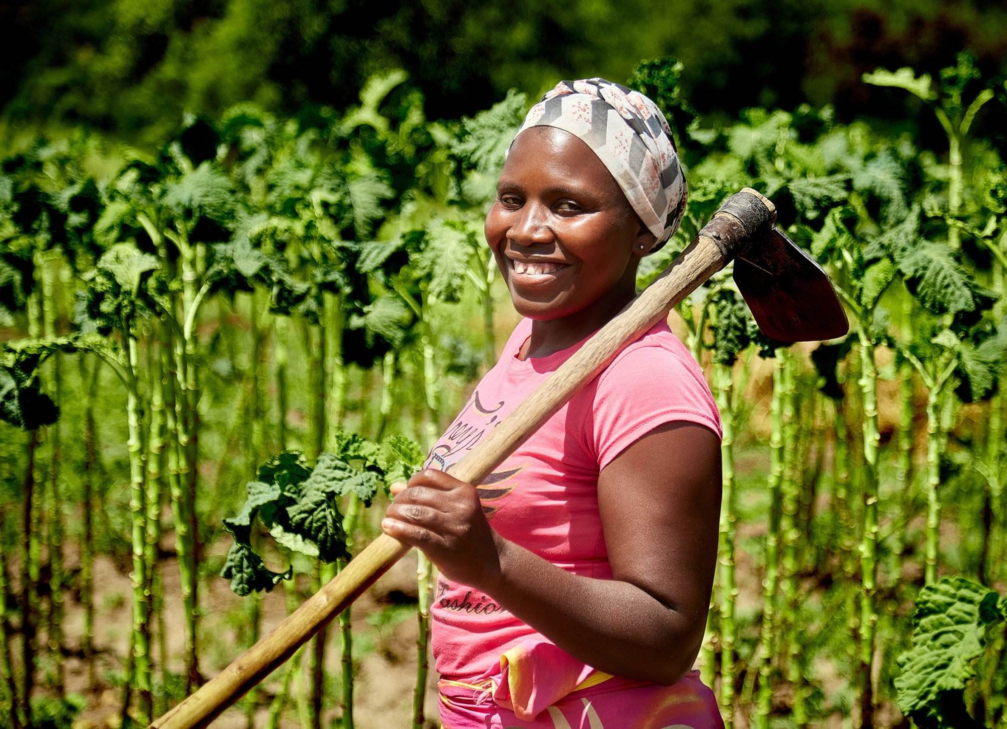 A smiling woman holding an ax in a field, showcasing farming that works with resources effectively.
