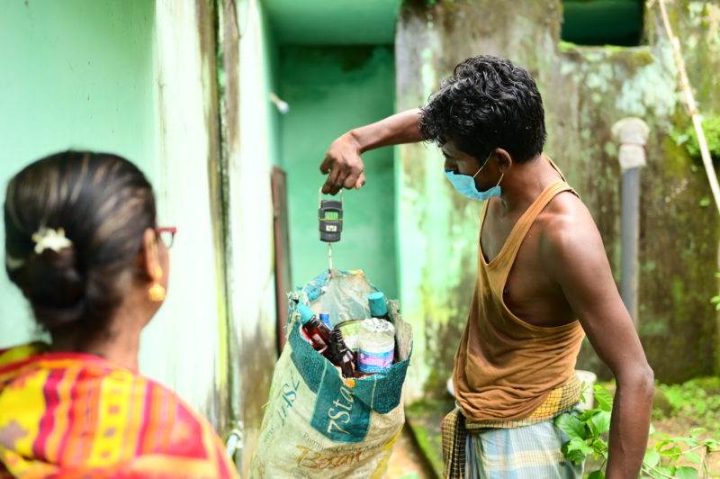A man practicing waste management holds a bag of water while wearing a face mask.
