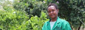 A woman in a green shirt standing in front of bushes