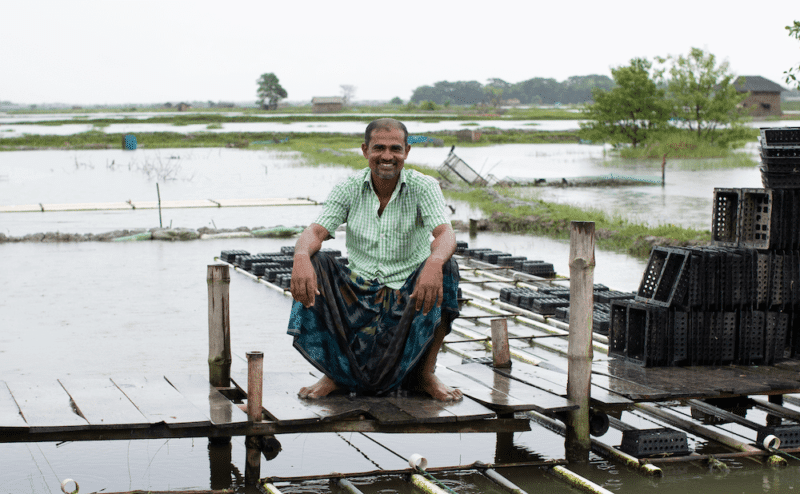 A man, Samakant, sitting on a wooden platform in a flooded area.