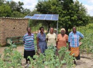 Four women exploring the links between energy access and climate change adaptation beside a solar panel.