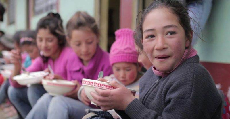 A group of children sitting on a bench, showcasing how waste products can improve livelihoods and the environment as they eat food.