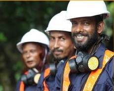 A group of men in hard hats and helmets are smiling, discussing the impact of plastic pollution in the ocean.