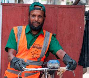 A man in an orange vest is standing next to a bicycle.