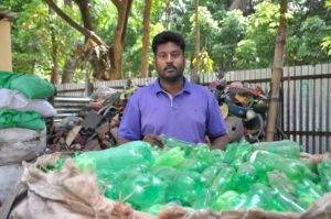 A man standing in front of a pile of green plastic bottles.
