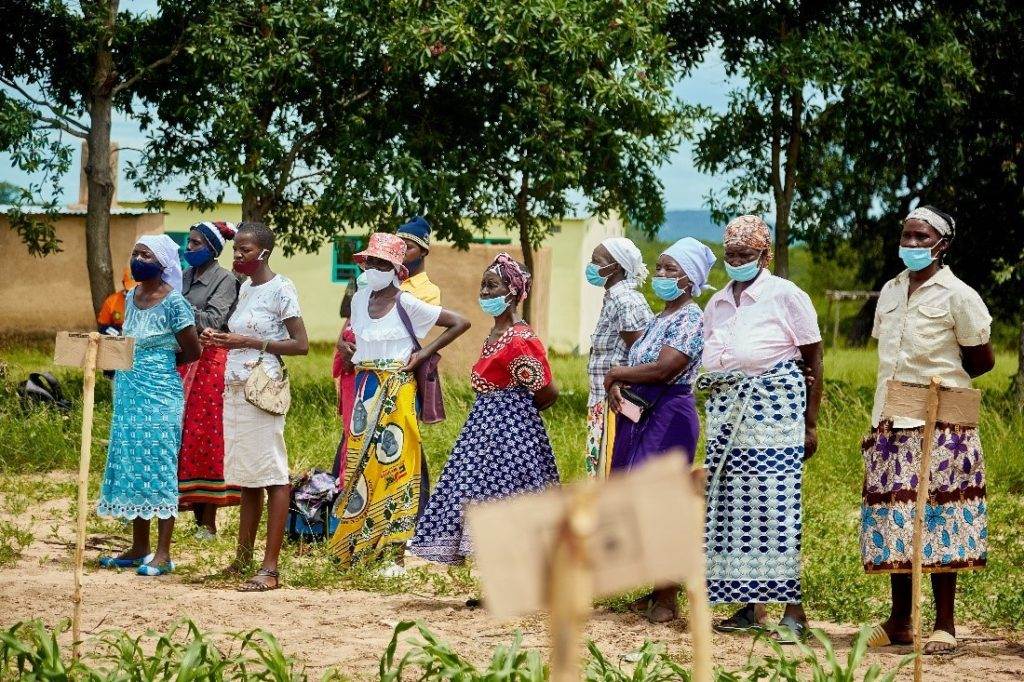 A group of Rwandan women farmers wearing face masks in a field stand up to climate change.