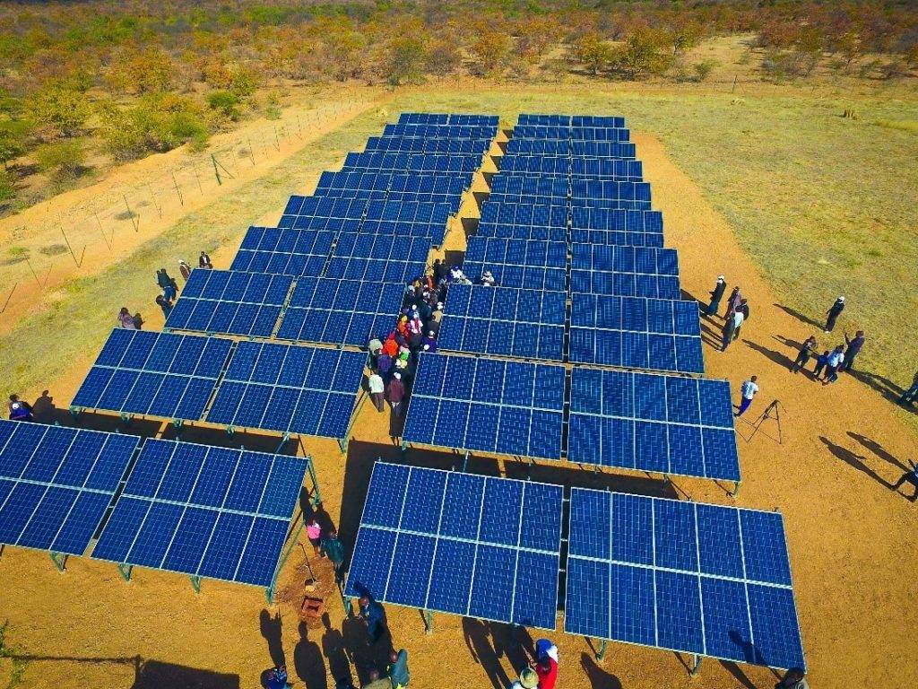 A group of Rwandan refugees and farmers standing in a field with solar panels.