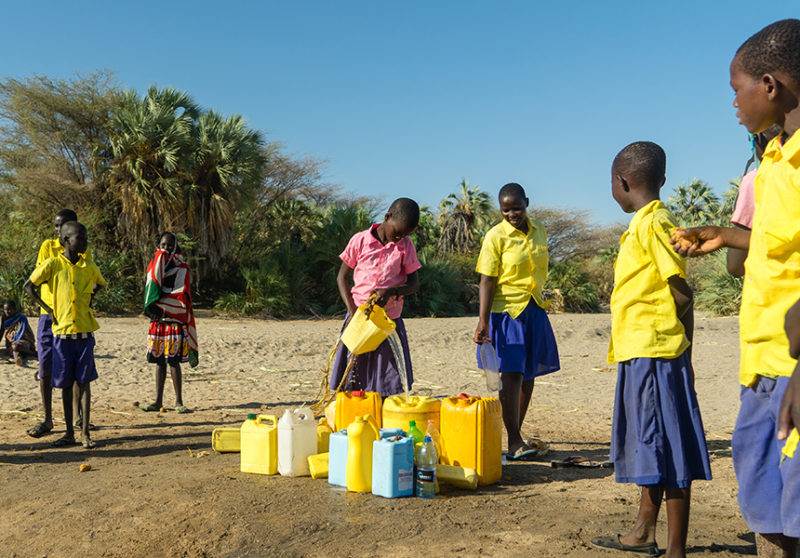 A group of children make every drop count as they stand around a water jug in an area where water is scarce.