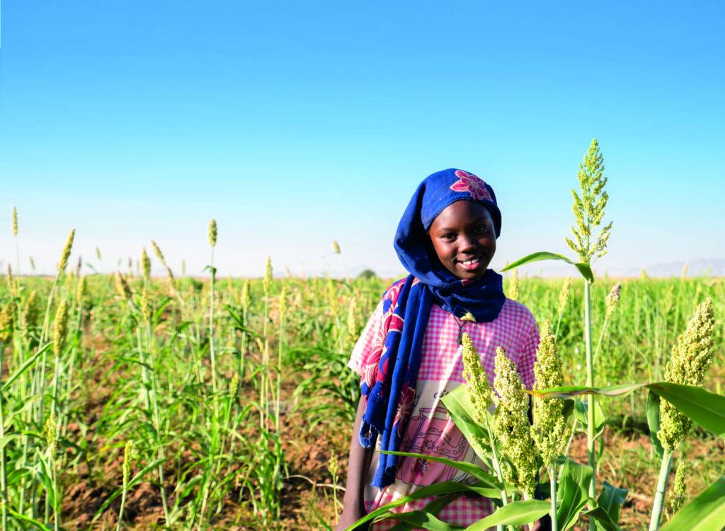A young girl standing in a field of wheat, smiling
