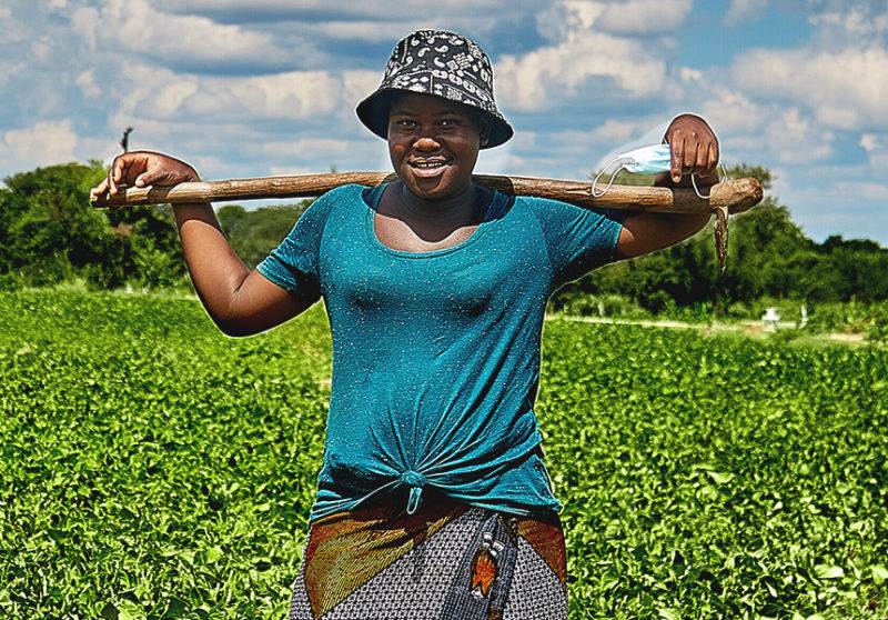 A woman holding a stick in a field where water is scarce.