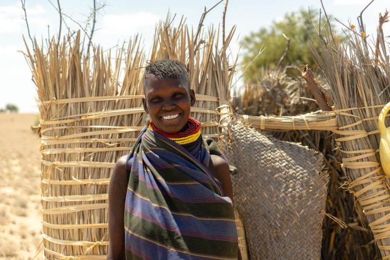 A young woman bridging science and practice for resilience standing in front of a straw hut.