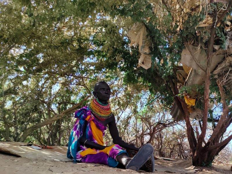 Narkruk Ikadeli from Turkana, Kenya sat under a tree, wearing colourful cultural dress