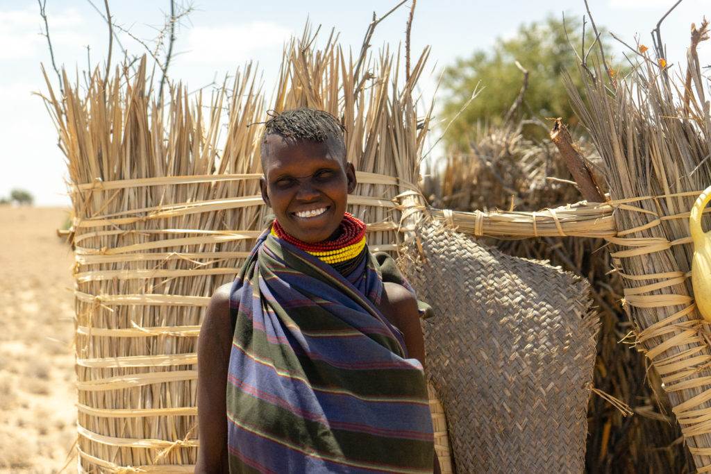 A young woman bridging science and practice for resilience while standing in front of a straw hut.