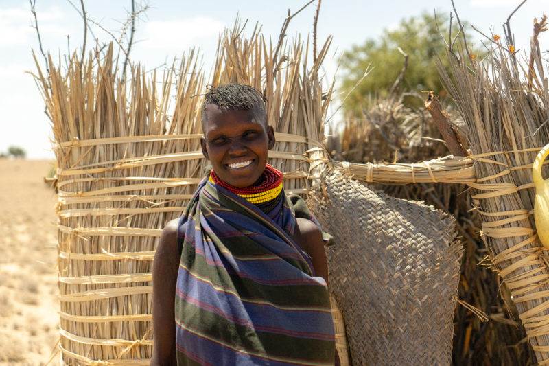 A young woman bridging science and practice for resilience while standing in front of a straw hut.