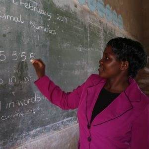A woman in a pink shirt is teaching about renewable energy sources on a blackboard.