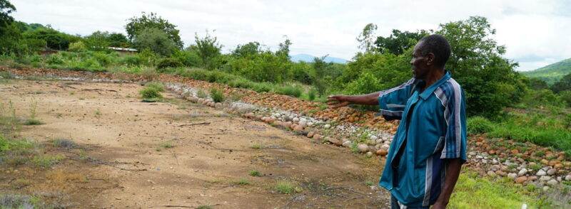 A man pointing to a dirt field in Chimanimani.