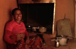 A woman conducting a decade-long funded project for clean cooking in Nepal, sits in front of a stove.