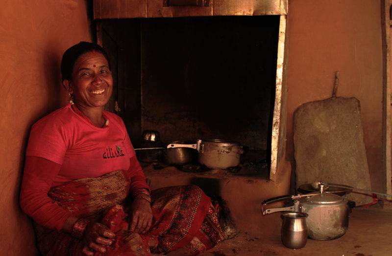 A woman conducting a decade-long funded project for clean cooking in Nepal, sits in front of a stove.