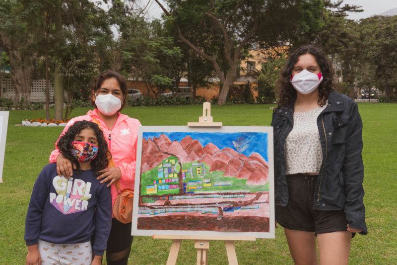 Peruvian community's art project wins global resilience award as three women wearing face masks stand next to a painting easel.