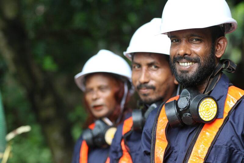 A group of men in hard hats are smiling while working on faecal sludge management.