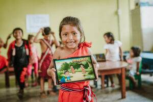 A girl from Peru is holding up an iPad in front of a classroom during a practical action.