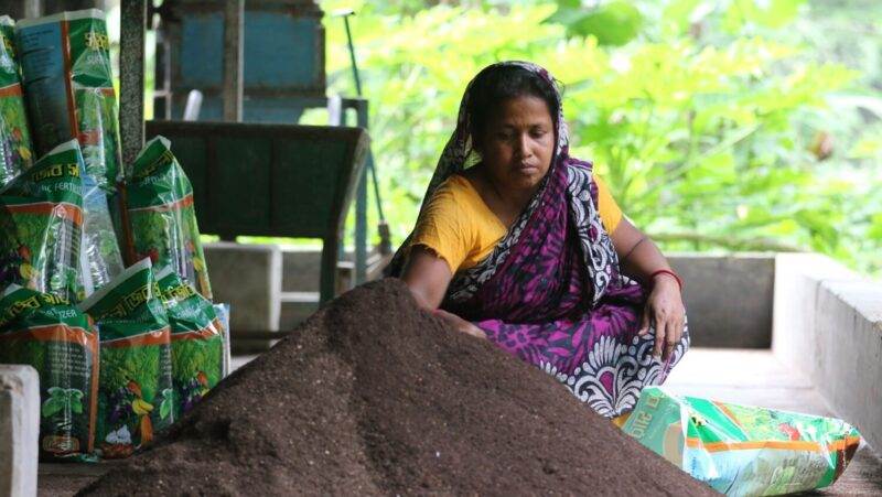 A woman manages faecal sludge next to a pile of soil.