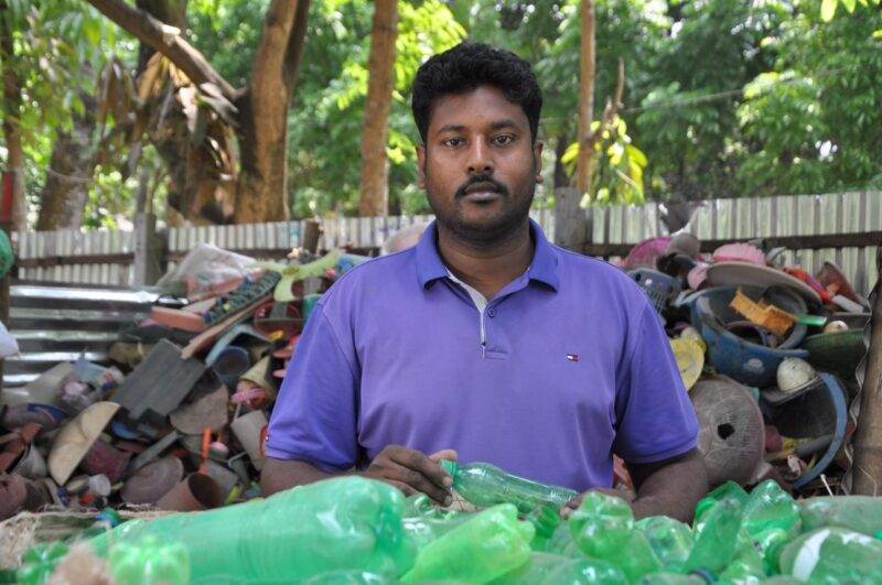 A man championing a people-centred approach to the growing waste crisis with a pile of green plastic bottles.