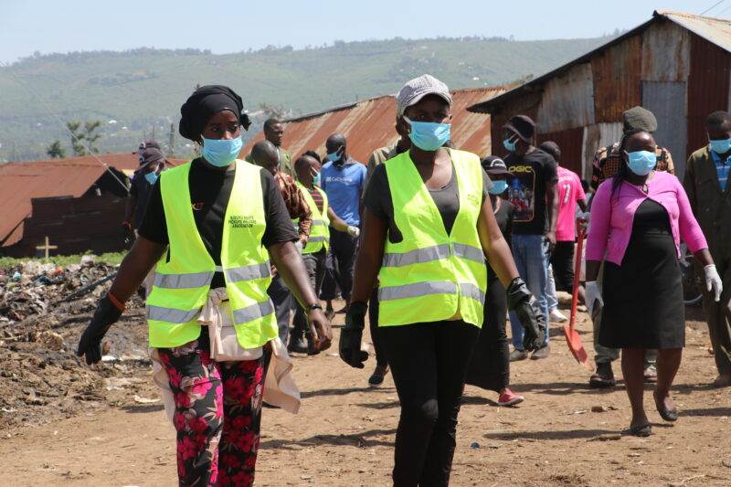A group of people managing waste while walking down a dirt road.