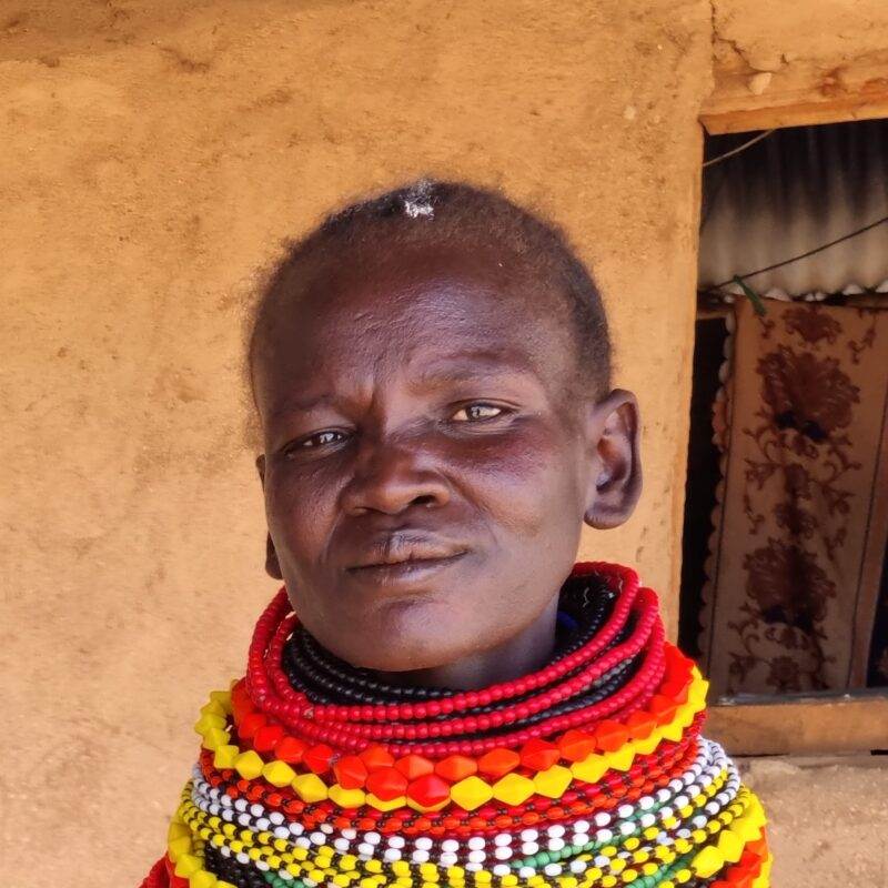 A woman wearing colorful beads in front of a house seeks long-term solutions to help people thrive.