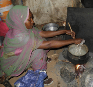 A woman is practicing clean cooking in a hut.