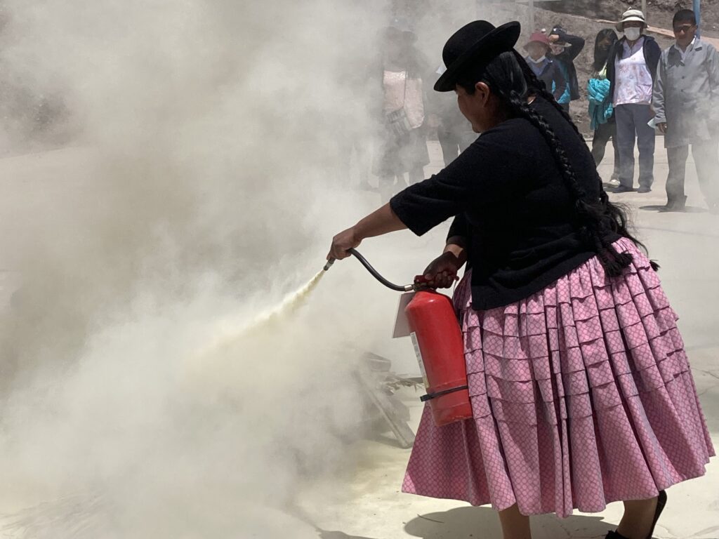 A woman sprays a cloud of smoke while wearing a skirt and a hat.