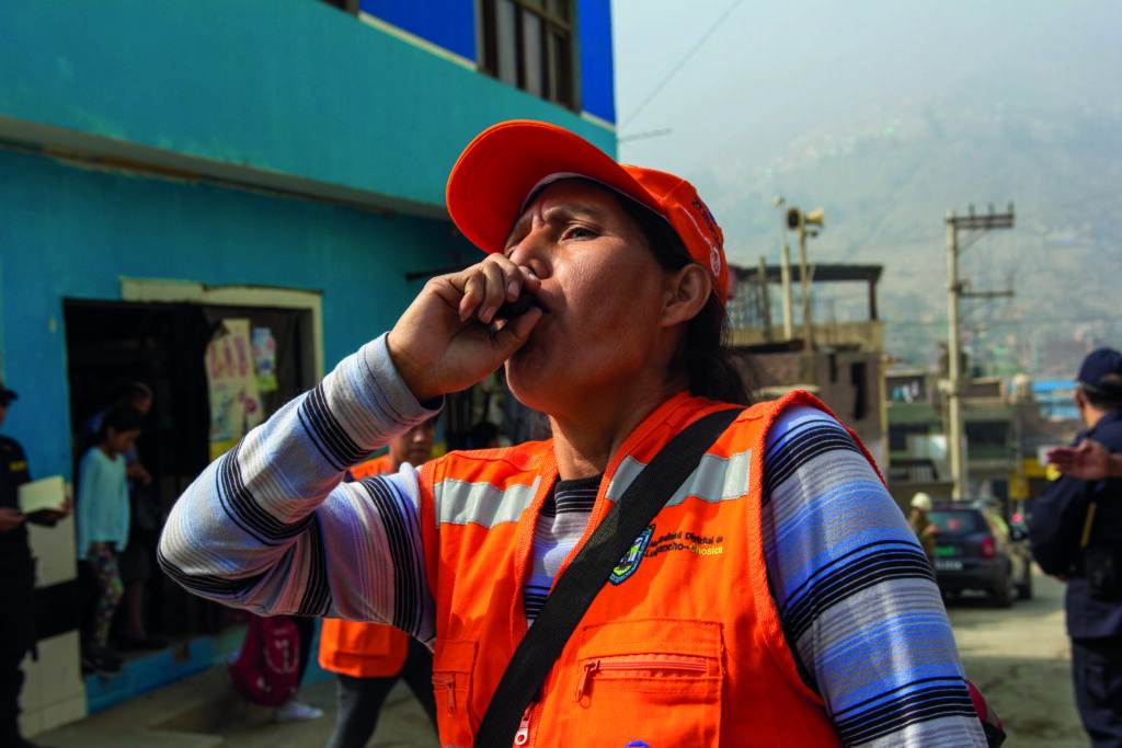 An image: Deborah blows a whistle during a disaster resilience training exercise. She volunteers in the local ‘brigade’, helping to give her community vital early warnings in the face of destructive floods and landslides.