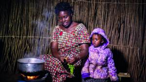 An image: Gentille purchased a clean cookstove through the Renewable Energy for Refugees project in Rwanda. The reduced smoke emitted means her family’s health has improved. She can also cook a lot faster, giving her more time with her children.