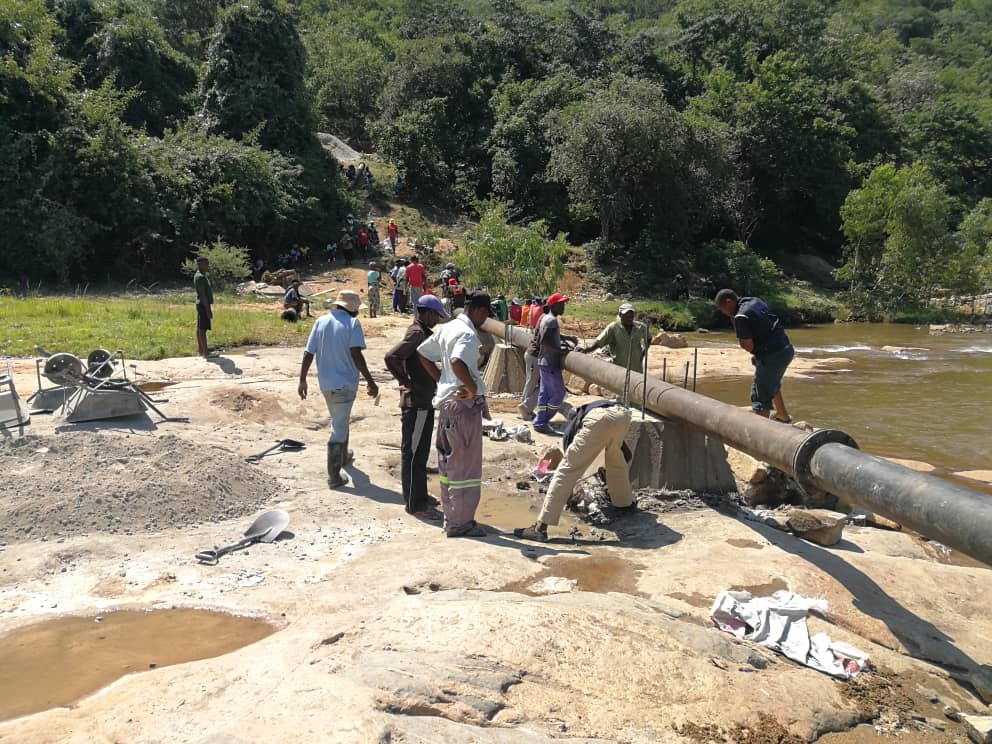 Practical Action in Zimbabwe working on a pipe near a river.