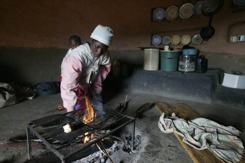 A woman is cooking on an open fire in a small kitchen.