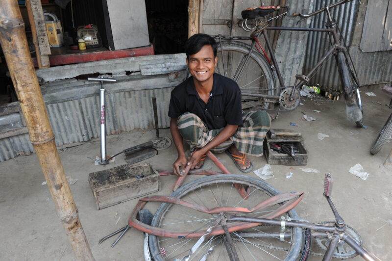 A man sitting on the ground next to a small bicycle after half a decade.