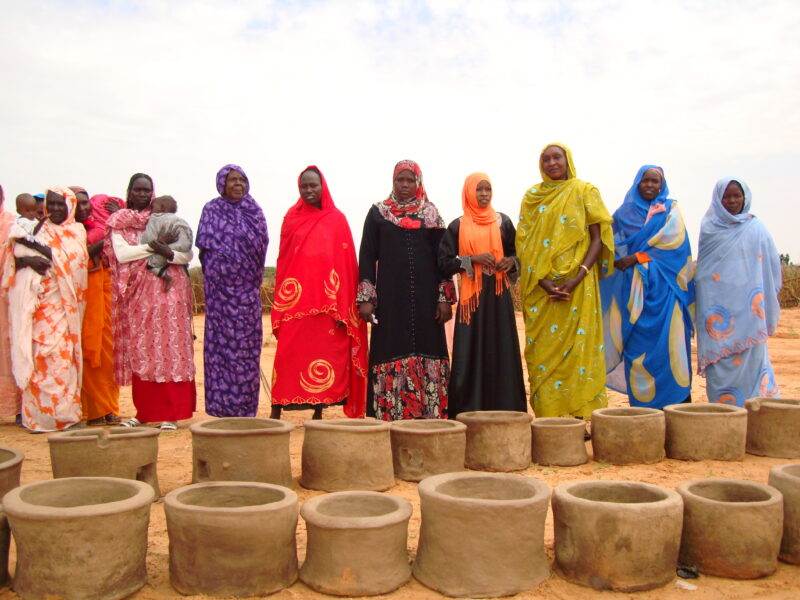 A group of women standing in front of a group of small pots.