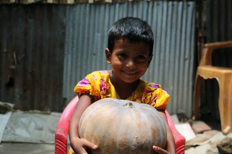A small child holding a large pumpkin.