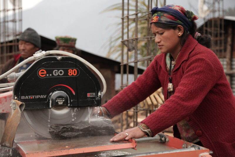 A woman is using a small saw to cut concrete.