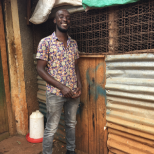 A man stands in front of a shack during a field visit.