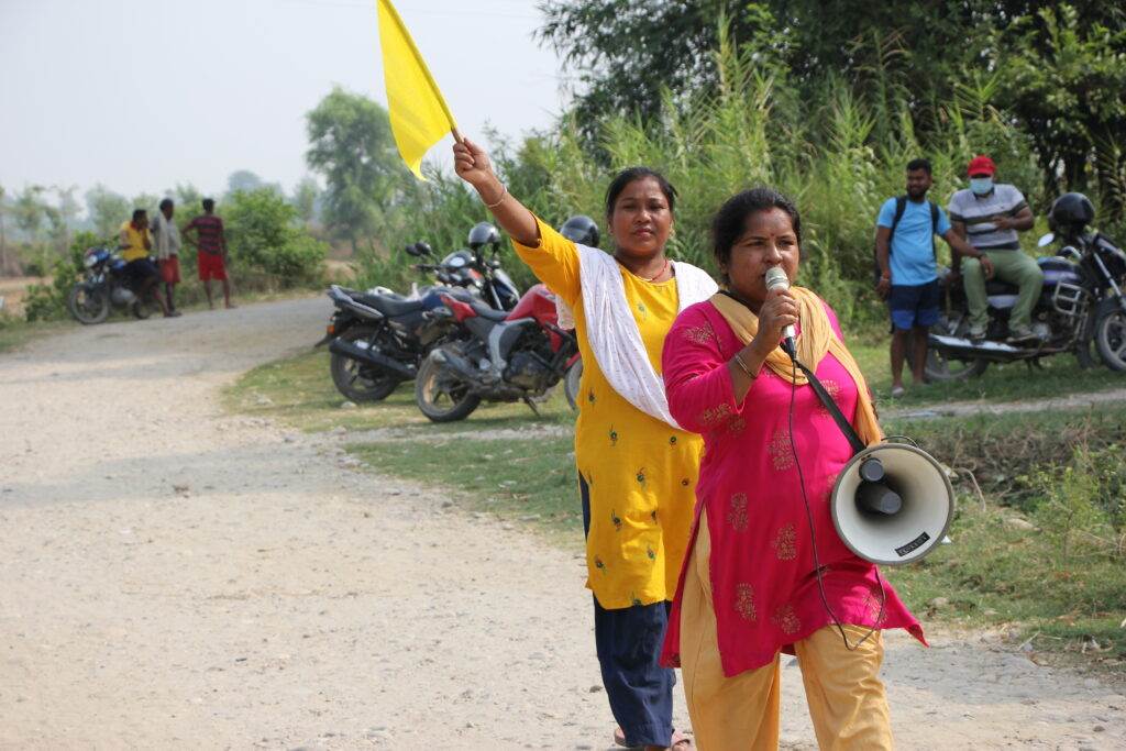 Two women from Practical Action in Nepal walking down a dirt road with a megaphone.