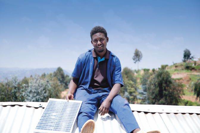 A man sitting on top of a roof, harnessing solar power to transform and empower lives.