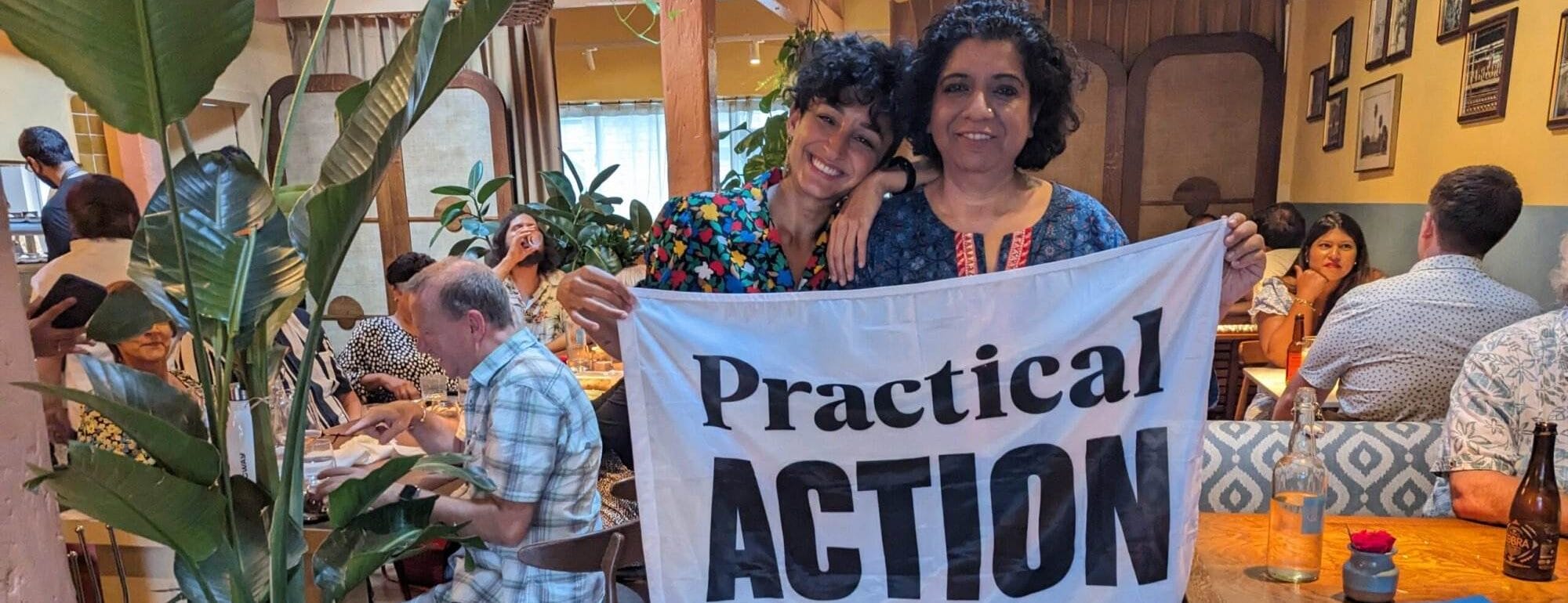 Two people holding up a sign that says practical action at a Supper Club Success event.